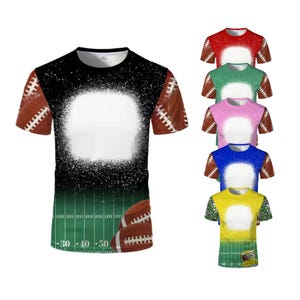 Puede incluir: Una camiseta de manga corta con temática de fútbol americano. La camiseta presenta un fondo negro y verde con un círculo blanco en el centro. Balones de fútbol en las mangas y en la parte inferior. También se muestran camisetas adicionales en rojo, verde, rosa, azul y amarillo.