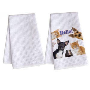 Puede incluir: Dos paños de cocina blancos con tejido de gofre. Uno presenta una impresión de varias mascotas, incluyendo gatos, un perro y un conejillo de indias, con la palabra "Hello!". El otro paño es blanco liso.