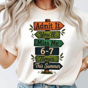May include: Cream-colored t-shirt featuring a graphic of wooden signposts. The signs read "Admit It", "You'll Miss Me", "6-7 Times", and "This Summer". The signs are in shades of orange, green, and blue.