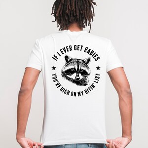 May include: White t-shirt with a black and white raccoon graphic. The text around the raccoon reads "If I Ever Get Rabies, You're High On My Bitin' List."