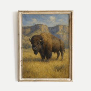 May include: Framed vintage painting of a bison standing in a field of tall grass. The bison is brown with large horns, set against a backdrop of mountains and a blue sky. The frame is a light, distressed wood.