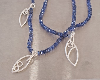 May include: Two silver necklaces with blue gemstone beads and silver leaf-shaped pendants. The pendants have an openwork design.
