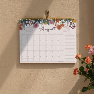 May include: A wall calendar for the month of August featuring a floral illustration at the top with pink, orange, and yellow flowers. The calendar has a grid layout with days of the week, a notes section on the right, and gold spiral binding.