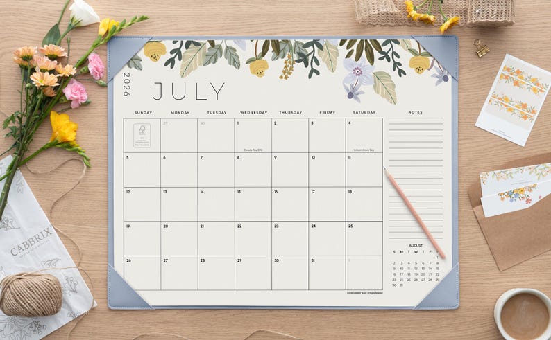 K&ouml;nnte beinhalten: Ein Schreibtischkalender f&uuml;r Juli 2026 mit einer floralen Illustration aus gelben und violetten Blumen am oberen Rand. Der Kalender hat ein Rasterlayout mit einem Notizbereich auf der rechten Seite und hellblauen Eckschonern.