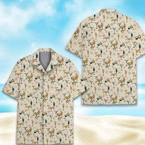 May include: Two short-sleeved button-down shirts with a cream background. The shirts display a repeating pattern of cocktail glasses, koalas, and starbursts in orange, yellow, blue, and brown. The shirts are on a sandy beach with a blue sky.