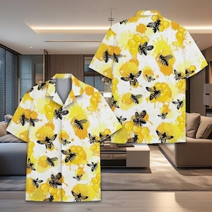 May include: A short-sleeved button-down shirt featuring a repeating pattern of black bees and yellow honeycomb designs on a white background. The shirt has a classic collar and is displayed in two views, front and back.