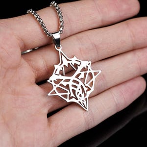 May include: A silver-colored pendant necklace featuring a geometric, star-like design. The pendant is suspended from a matching chain. The necklace is displayed on an open hand against a dark background.