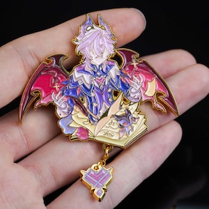 May include: A detailed enamel pin featuring a character with purple hair, wings, and a heart-shaped pendant. The pin has a gold outline and depicts the character with a book and a small creature. The wings are red and pink.