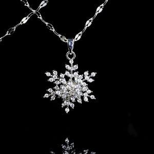 Könnte beinhalten: Eine silberne Halskette mit einem Schneeflocken-Anhänger. Der Anhänger ist mit zahlreichen klaren, funkelnden Kristallen besetzt, die einen schillernden Effekt erzeugen. Die Kette hat ein filigranes, verbundenes Design. Der Hintergrund ist tiefschwarz.