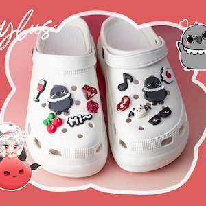 Könnte beinhalten: Weiße Clogs, verziert mit verschiedenen Charms, darunter eine Musiknote, ein Weinglas, ein Diamant und ein Cartoon-Vogel. Das Wort "stylus" ist in Kursivschrift oben links geschrieben. Der Hintergrund ist hellrot.