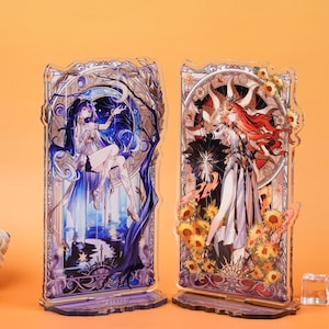 May include: Two acrylic display stands featuring anime-style illustrations. One depicts a woman in a blue and white dress against a night sky, the other a woman in a white dress with red hair and sunflowers. Both have decorative frames.