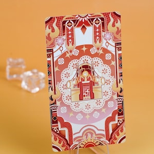 Puede incluir: Una tarjeta decorativa con una ilustraci&oacute;n detallada de un trono en tonos rojos, naranjas y crema. La tarjeta tiene un dise&ntilde;o sim&eacute;trico con motivos florales y en forma de llama. La tarjeta se muestra sobre un soporte transparente sobre un fondo naranja.