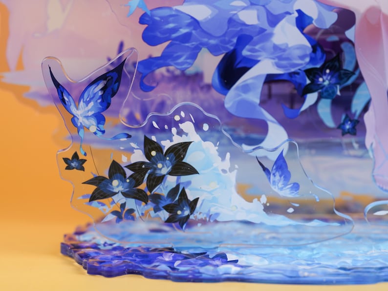 Op de afbeelding: Een decoratieve acryl display met een blauw-wit aquatisch thema. Het ontwerp bevat vlinders, bloemen en waterelementen. De basis heeft een golvend, gestructureerd ontwerp.