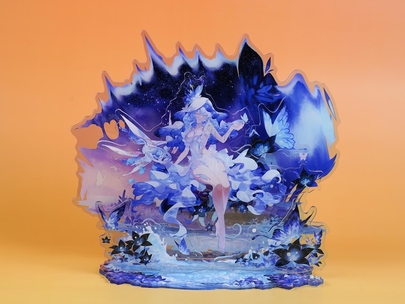 Op de afbeelding: Decoratieve acrylfiguur met een fantasie-illustratie. Het kunstwerk toont een vrouw in een vloeiende jurk met blauwe en witte accenten, omringd door vlinders en bloemelementen. Het kleurenpalet omvat tinten blauw, wit en paars.