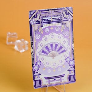 Puede incluir: Una tarjeta rectangular con un dise&ntilde;o de inspiraci&oacute;n japonesa en tonos morados y blancos. La tarjeta presenta un abanico, flores de cerezo y elementos arquitect&oacute;nicos. El fondo es de color naranja liso.