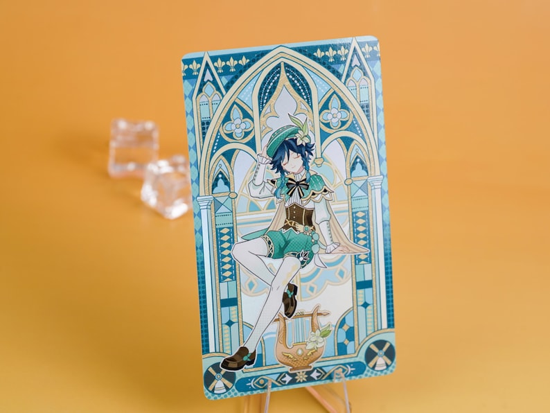 Puede incluir: Una tarjeta rectangular con una ilustraci&oacute;n de personaje. El personaje viste un atuendo verde y blanco, sentado frente a un arco decorativo. La tarjeta tiene una combinaci&oacute;n de colores azul y dorado, con una lira en la parte inferior. La tarjeta est&aacute; apoyada.