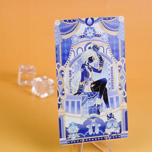 Puede incluir: Una tarjeta ilustrada en azul y blanco que presenta una figura sentada con cabello blanco y una silueta oscura. La tarjeta est&aacute; apoyada en un soporte transparente sobre un fondo naranja. Dos objetos transparentes en forma de cubo est&aacute;n en el fondo.