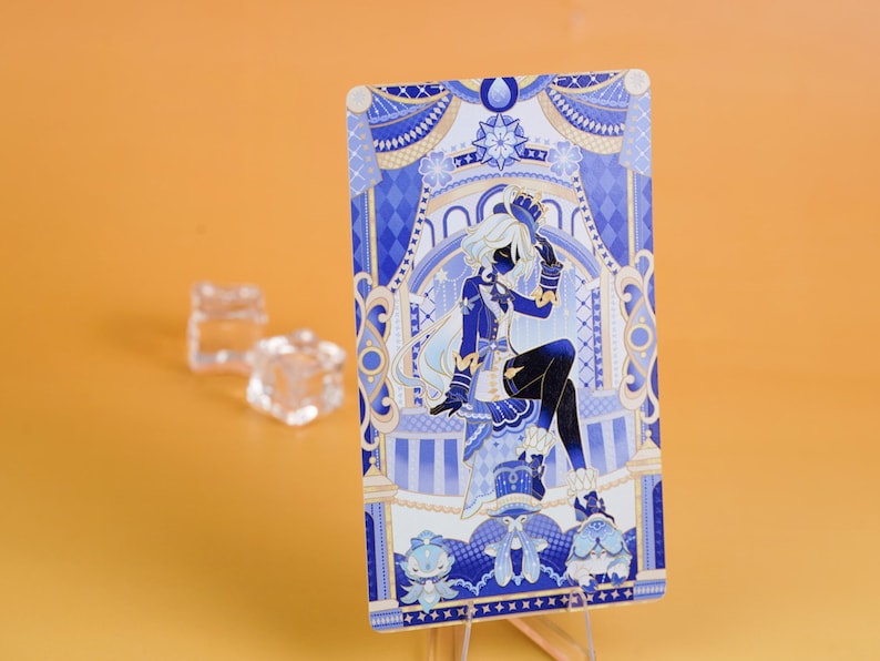 Puede incluir: Una tarjeta ilustrada en azul y blanco que presenta una figura sentada con cabello blanco y una silueta oscura. La tarjeta est&aacute; apoyada en un soporte transparente sobre un fondo naranja. Dos objetos transparentes en forma de cubo est&aacute;n en el fondo.