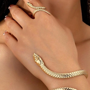 May include: Gold-colored snake ring and bracelet set. The ring wraps around a finger, and the bracelet encircles the wrist. Both pieces feature a textured, scale-like pattern and snake head details.