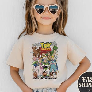 Puede incluir: Una camiseta beige con un gr&aacute;fico colorido de personajes de la pel&iacute;cula animada "Toy Story". La camiseta tiene el texto "Toy Story" en la parte superior y "You've Got a Friend in Me" en la parte inferior. La imagen tambi&eacute;n incluye un gr&aacute;fico de "Fast Shipping".