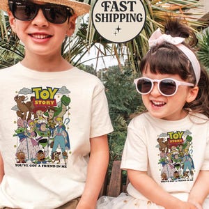Puede incluir: Dos ni&ntilde;os con camisetas color crema con un gr&aacute;fico colorido de personajes de Toy Story. Las camisetas tienen el texto "TOY STORY" y "YOU'VE GOT A FRIEND IN ME". El ni&ntilde;o lleva gafas de sol y un sombrero de paja. La ni&ntilde;a lleva gafas de sol y un lazo rosa.