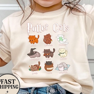 May include: Cream-colored t-shirt featuring the text "Potter Cats" above nine cartoon cat illustrations. Each cat is depicted in a different pose and color, with various accessories. A round "Fast Shipping" graphic is at the bottom.