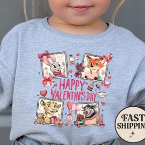 May include: A light gray sweatshirt featuring four framed cartoon characters with Valentine's Day themes. The words "HAPPY VALENTINE'S DAY" are printed in pink. A "FAST SHIPPING" graphic is on the bottom right.