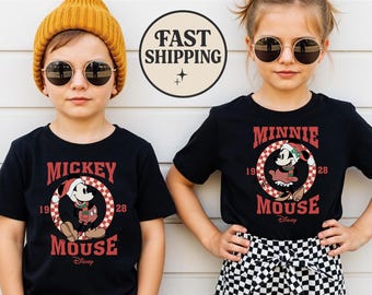 May include: Two children wearing black t-shirts with Mickey and Minnie Mouse graphics. The Mickey Mouse shirt has a red and white checkered design around the character. The Minnie Mouse shirt has a similar design. Both shirts have the text "1928" and "Mouse" in red.
