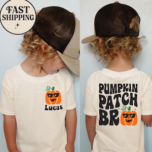 Może przedstawiać: Kremowa koszulka z grafiką dyni w okularach przeciwsłonecznych i imieniem "Lucas" wydrukowanym poniżej. Tył koszulki mówi "Pumpkin Patch Bro" z grafiką dyni. Noszona jest brązowo-beżowa czapka typu trucker.