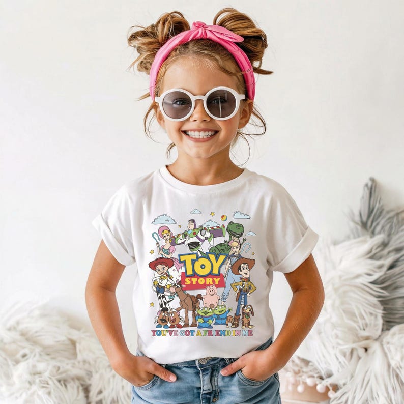 Op de afbeelding: Een wit T-shirt met een kleurrijke afbeelding van personages uit de animatiefilm "Toy Story". Het shirt heeft de woorden "Toy Story" in grote gele en blauwe letters, met de zin "You've Got a Friend in Me" eronder.