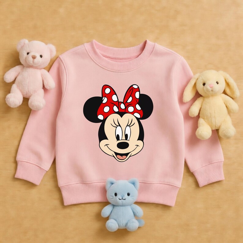 Może przedstawiać: Jasnor&oacute;żowa bluza z nadrukiem Myszki Minnie z czerwoną kokardą w białe grochy. Na zdjęciu r&oacute;żowy miś, ż&oacute;łty kr&oacute;lik i niebieski pluszowy kot.