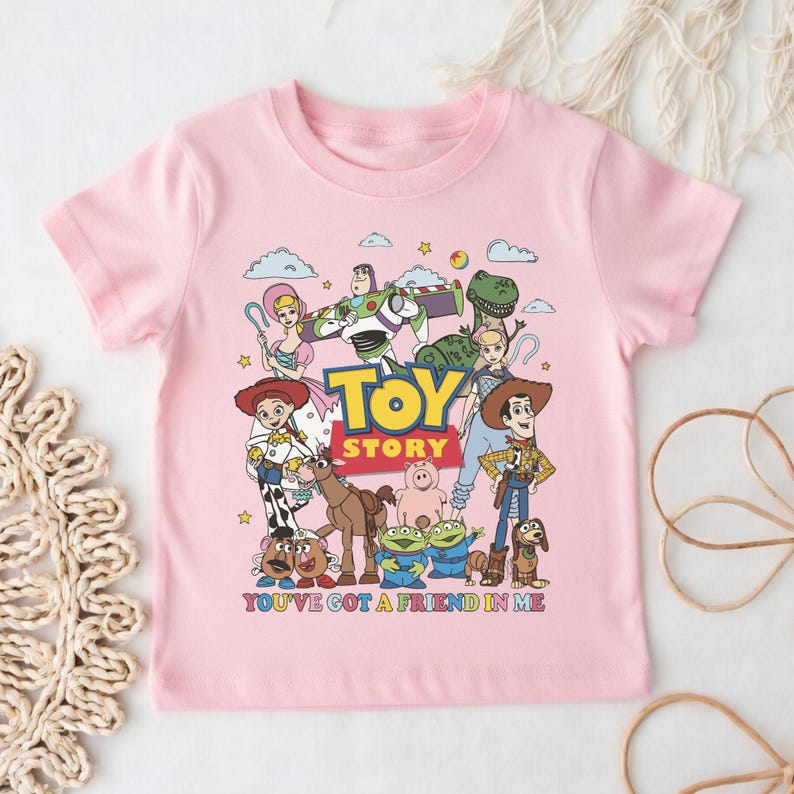 Op de afbeelding: Roze T-shirt met korte mouwen met een kleurrijke afbeelding van personages uit de animatiefilm "Toy Story". Het ontwerp bevat de titel van de film en de zin "You've Got a Friend in Me".