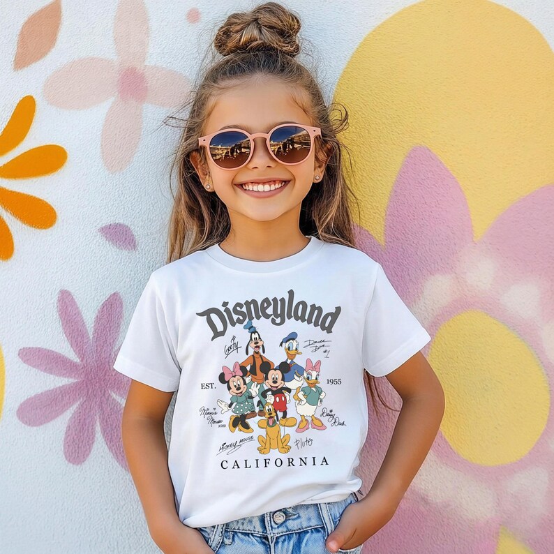 May include: White t-shirt featuring the Disneyland logo and cartoon characters, including Mickey and Minnie Mouse, Goofy, Donald and Daisy Duck. The shirt also has the text "CALIFORNIA" and "EST. 1955".
