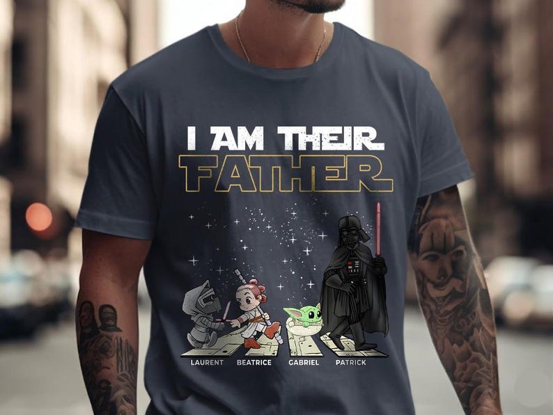 May include: Navy blue t-shirt with the text "I AM THEIR FATHER" in white and gold. The shirt features cartoon illustrations of Star Wars characters, including Darth Vader, and the names Laurent, Beatrice, Gabriel, and Patrick.