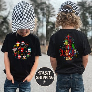Może przedstawiać: Czarny t-shirt z świątecznym wzorem z postaciami Marvela w czapkach Świętego Mikołaja i lampkami choinkowymi. Tył koszulki przedstawia choinkę z postaci Marvela. Dziecko ma na sobie czarno-białą czapkę w szachownicę.