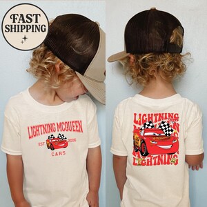 Puede incluir: Una camiseta color crema con Lightning McQueen de la pel&iacute;cula Cars. El gr&aacute;fico frontal incluye el texto "Lightning McQueen" y un coche de carreras. La parte posterior de la camiseta tiene una imagen m&aacute;s grande de Lightning McQueen con banderas a cuadros.