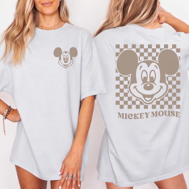 May include: Light blue t-shirts featuring a Mickey Mouse graphic. The front of the shirt has a small Mickey Mouse face, while the back has a larger Mickey Mouse face within a checkered pattern. The words "Mickey Mouse" are printed below the graphic.