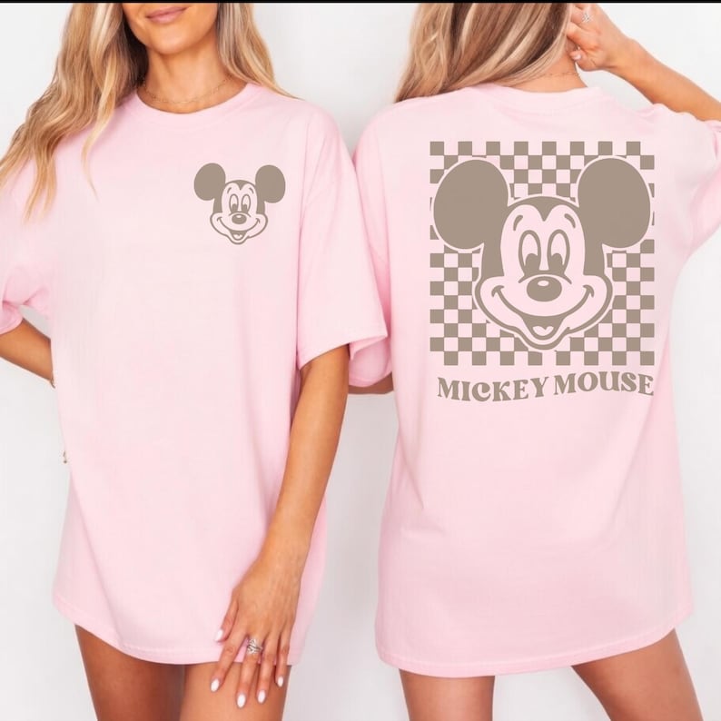 May include: Light pink t-shirts featuring a Mickey Mouse graphic. One shirt has a small Mickey Mouse on the front, the other has a larger Mickey Mouse design on the back with a checkered background and the words "Mickey Mouse".
