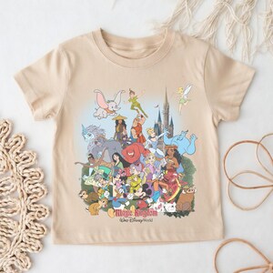 May include: Beige short-sleeved t-shirt featuring a colorful graphic of Disney characters, including Mickey Mouse, Dumbo, and Peter Pan. The text "Magic Kingdom Walt Disney World" is printed at the bottom of the design.