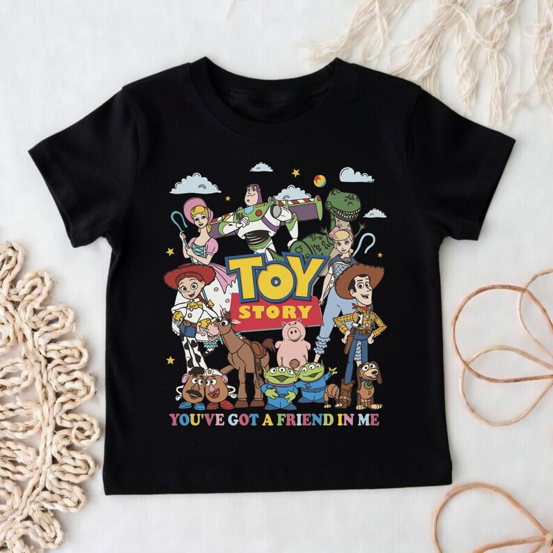 Op de afbeelding: Zwart T-shirt met een kleurrijke afbeelding van personages uit de animatiefilm "Toy Story". Het ontwerp bevat Woody, Buzz Lightyear en andere personages, met de tekst "TOY STORY" en "YOU'VE GOT A FRIEND IN ME."