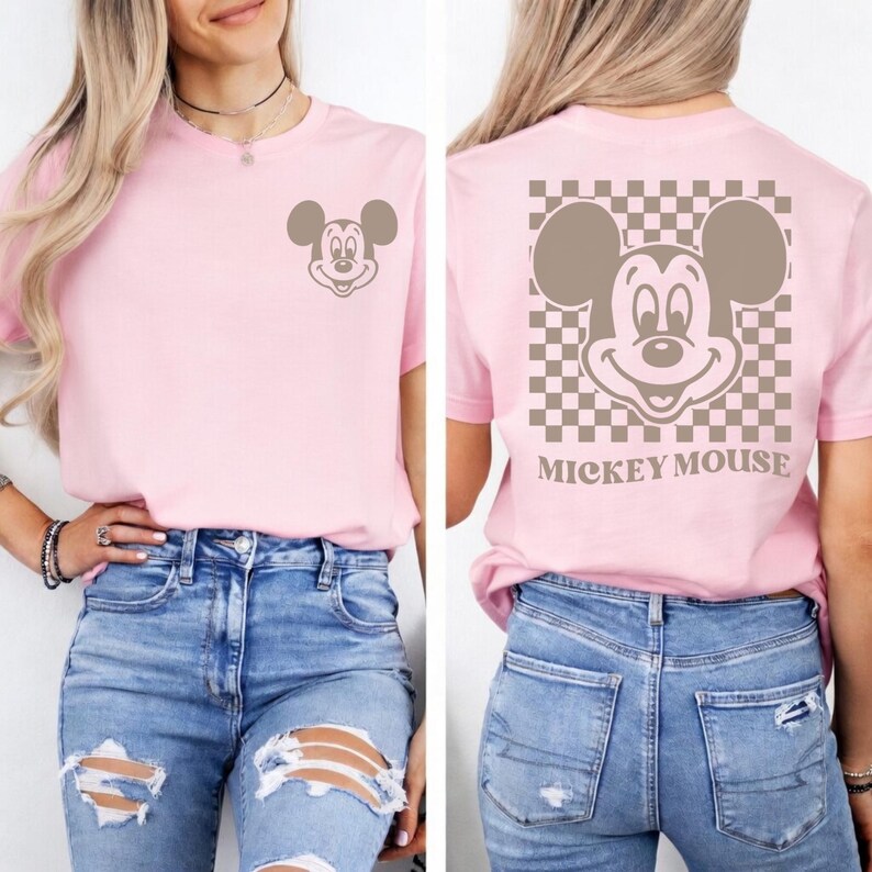 May include: A light pink t-shirt featuring a Mickey Mouse graphic on the front and back. The front has a small Mickey Mouse head, while the back has a larger Mickey Mouse face with a checkered background and the words "Mickey Mouse".