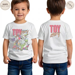 May include: White t-shirt featuring the words "TOY STORY" in pink and orange, with a graphic of Woody, Buzz Lightyear, and Rex. The front of the shirt has the text "SINCE 1995". The back of the shirt has the words "TOY STORY".