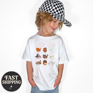 May include: A white t-shirt featuring the text "Potter Cats" above a grid of cartoon cat illustrations. The cats are in various colors and poses. The person is wearing a black and white checkered baseball cap.