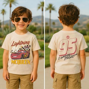 May include: Tan t-shirt featuring Lightning McQueen from the Cars movie. The front of the shirt displays the text "Lightning 95 McQueen" with a graphic of the race car. The back of the shirt has a large "95" and "Lightning McQueen" text.
