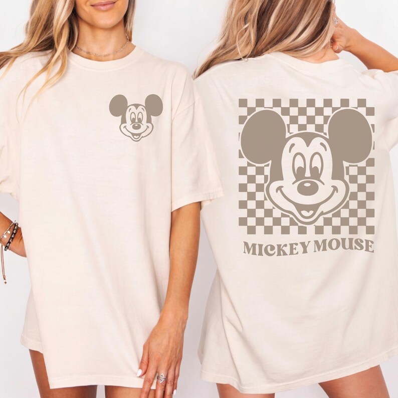 May include: Cream-colored t-shirt featuring a Mickey Mouse graphic. The front has a small Mickey face, while the back showcases a larger Mickey face on a checkered background with the words "Mickey Mouse" below.
