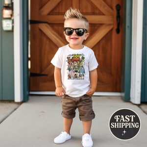 Puede incluir: Una camiseta blanca con un gr&aacute;fico colorido de personajes de "Toy Story" y el texto "TOY STORY" y "YOU'VE GOT A FRIEND IN ME". La camiseta se combina con pantalones cortos marrones y zapatillas blancas.