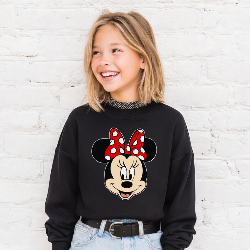 Może przedstawiać: Czarna bluza z nadrukiem Myszki Minnie. Grafika przedstawia twarz Myszki Minnie, czarne uszy i czerwoną kokardę w białe grochy. Bluza ma okrągły dekolt i długie rękawy.