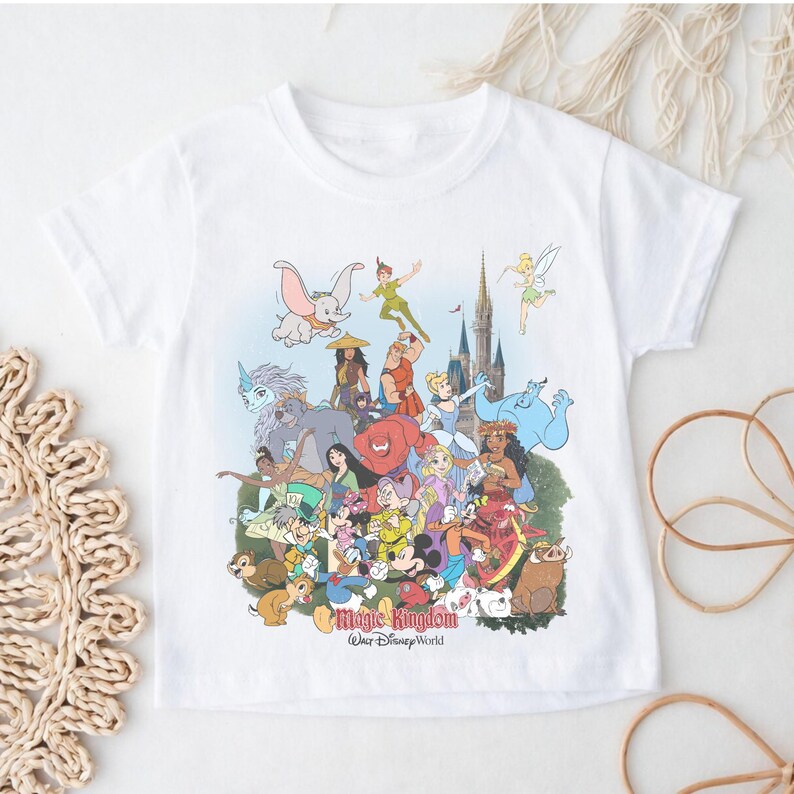 May include: White t-shirt featuring a colorful graphic of various Disney characters, including Dumbo, Peter Pan, and Mickey Mouse. The text "Magic Kingdom Walt Disney World" is printed at the bottom of the design. The shirt has short sleeves and a crew neck.
