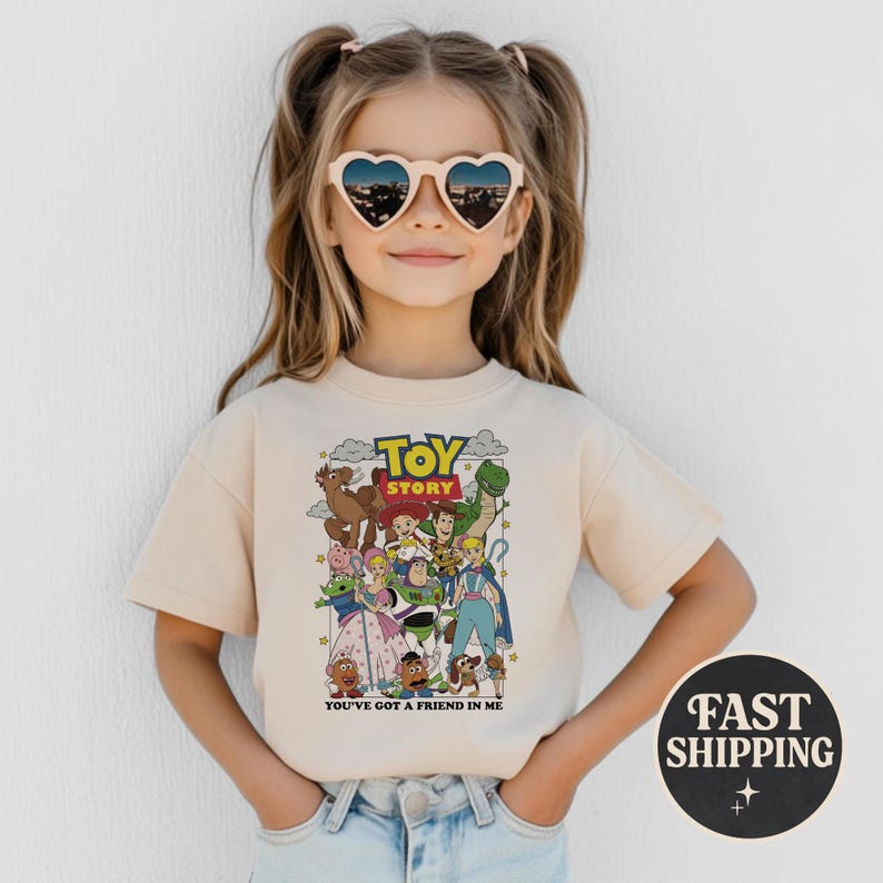 Puede incluir: Una camiseta beige con un gr&aacute;fico colorido de personajes de la pel&iacute;cula animada "Toy Story". La camiseta tiene el texto "Toy Story" en la parte superior y "You've Got a Friend in Me" en la parte inferior. La imagen tambi&eacute;n incluye un gr&aacute;fico de "Fast Shipping".