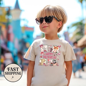 May include: A beige t-shirt featuring cartoon characters and the text "HAPPY VALENTINE'S DAY." The shirt has short sleeves and is worn by a child wearing sunglasses. The shirt has a graphic of cartoon characters.